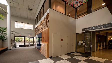 Before photo of the main entry of the UO Portland Campus Center. The left of the photo shows the entry doors, in the middle is a wall with an old art installation, on the left is the entry to the main dining room. 